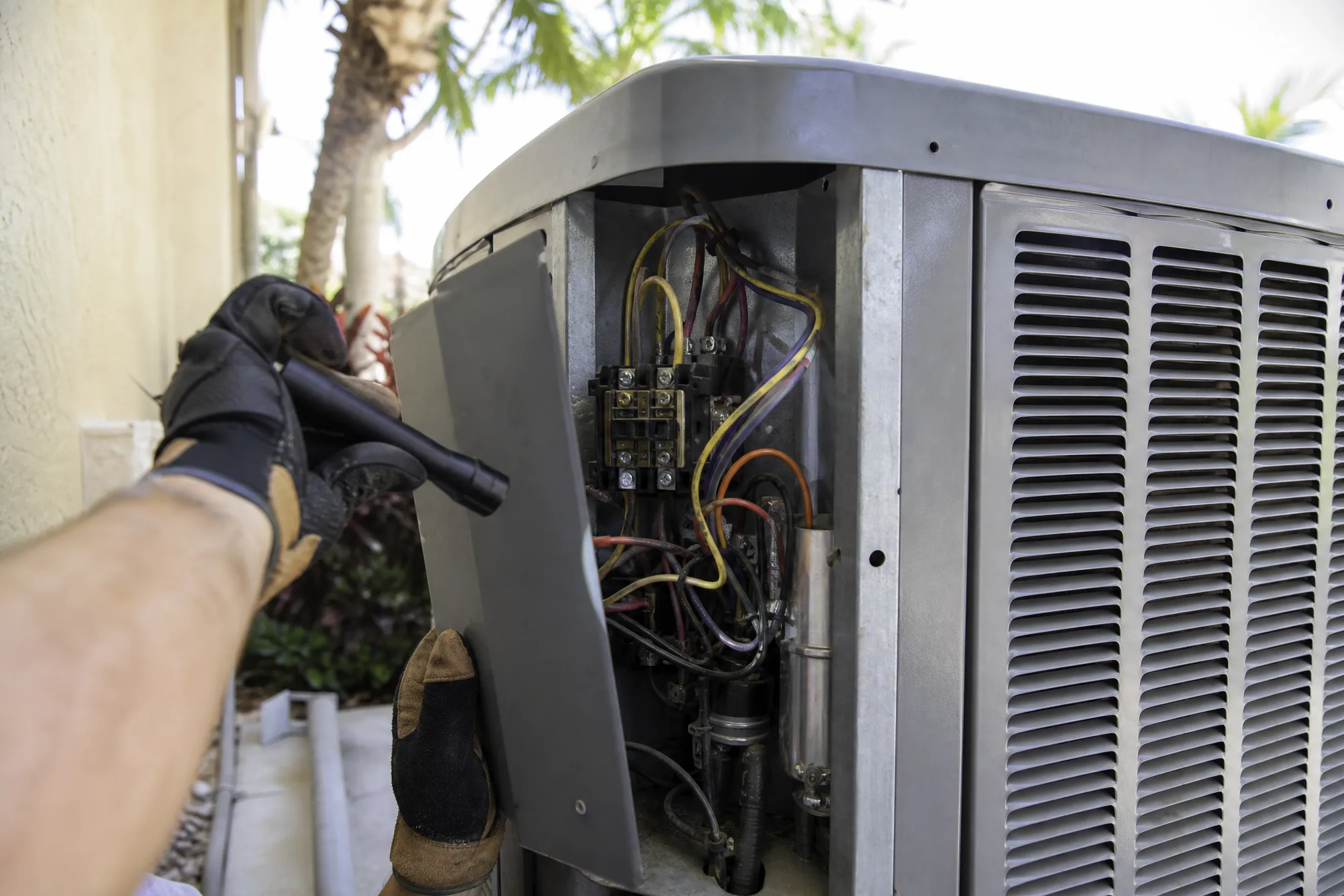 HVAC technician inspecting the electrical access panel of an outdoor AC condenser unit with a flashlight